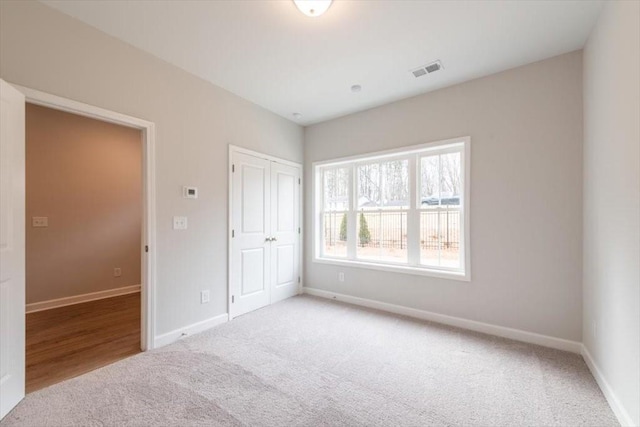 unfurnished bedroom with light colored carpet, visible vents, a closet, and baseboards