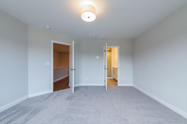 unfurnished bedroom with carpet flooring, ensuite bathroom, and baseboards