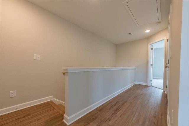 hallway with an upstairs landing, attic access, baseboards, and wood finished floors