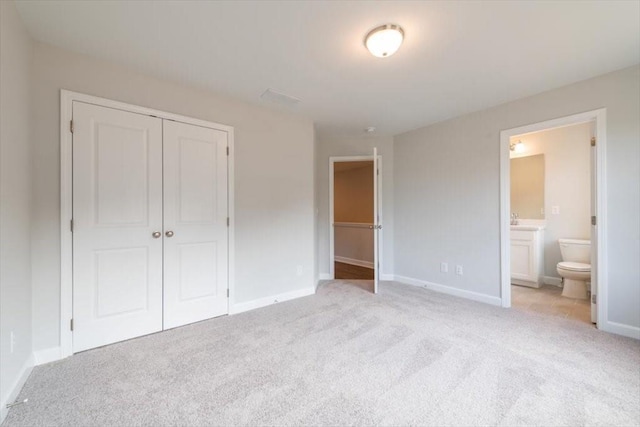 unfurnished bedroom featuring ensuite bath, baseboards, a closet, and light carpet