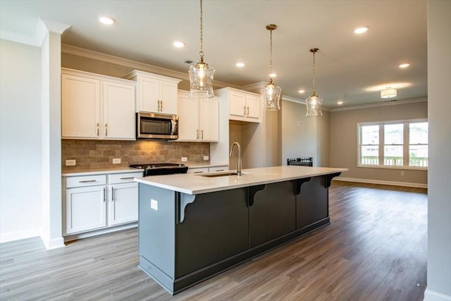 kitchen with stainless steel microwave, backsplash, a sink, range, and a kitchen island with sink