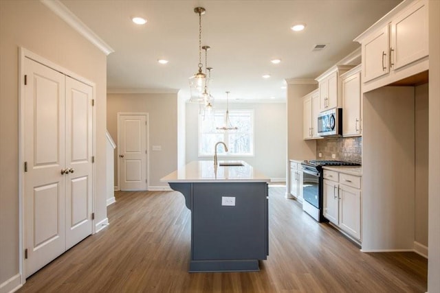 kitchen featuring a kitchen island with sink, a sink, appliances with stainless steel finishes, white cabinetry, and crown molding