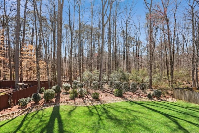 view of yard featuring a wooded view and fence