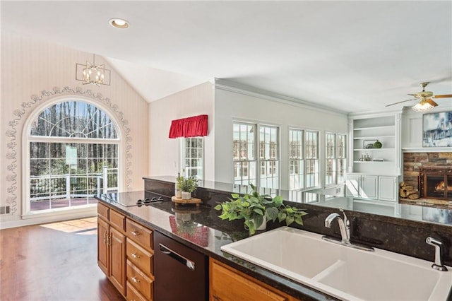 kitchen with wallpapered walls, vaulted ceiling, brown cabinets, black appliances, and a sink