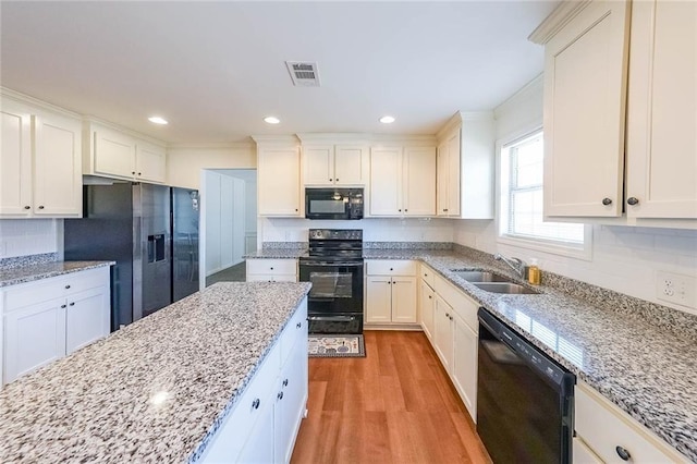 kitchen with light stone counters, light hardwood / wood-style floors, black appliances, and sink