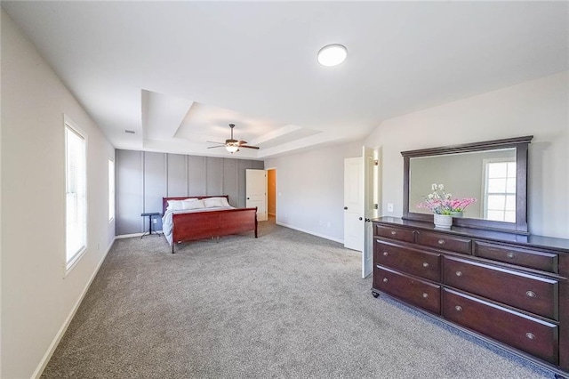 carpeted bedroom with ceiling fan and a tray ceiling