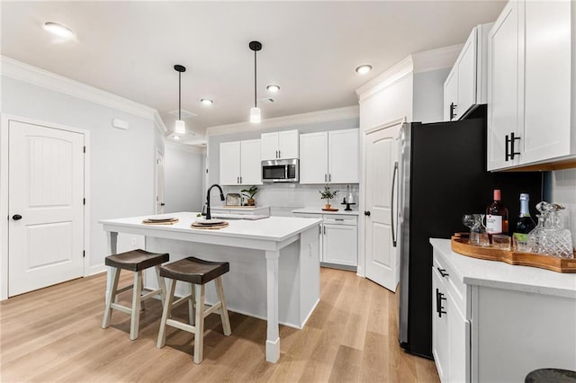 kitchen with tasteful backsplash, white cabinetry, a kitchen island with sink, light wood-type flooring, and pendant lighting