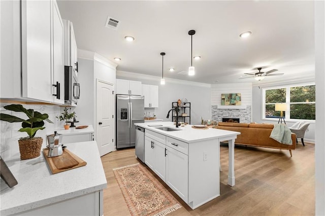 kitchen featuring white cabinets, appliances with stainless steel finishes, a kitchen island with sink, decorative light fixtures, and sink