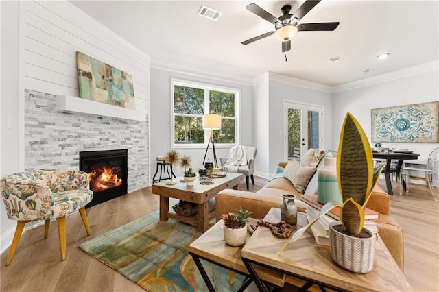 living room featuring crown molding, a stone fireplace, light hardwood / wood-style floors, and ceiling fan