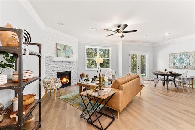 living room with light wood-type flooring, a fireplace, french doors, ceiling fan, and crown molding