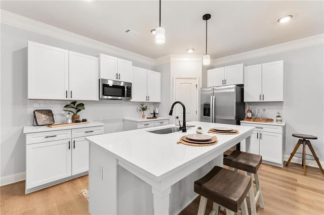 kitchen with appliances with stainless steel finishes, white cabinetry, decorative light fixtures, and a center island with sink