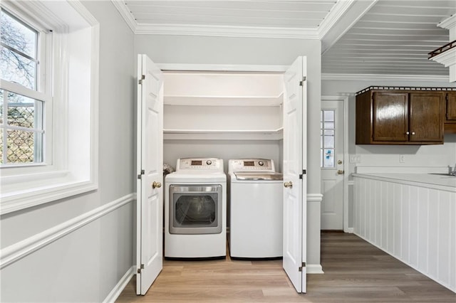 clothes washing area with washing machine and dryer, crown molding, and light hardwood / wood-style flooring