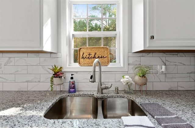 interior details featuring white cabinets, light stone counters, tasteful backsplash, and a sink