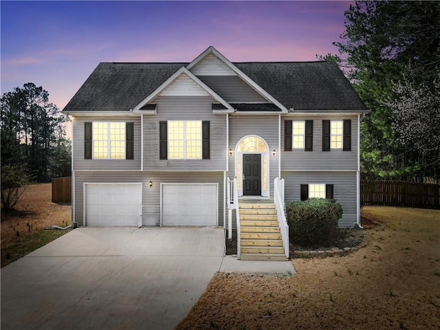 bi-level home with driveway, a shingled roof, a garage, and fence