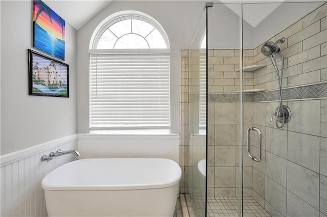 bathroom featuring vaulted ceiling, a freestanding tub, a stall shower, and wainscoting