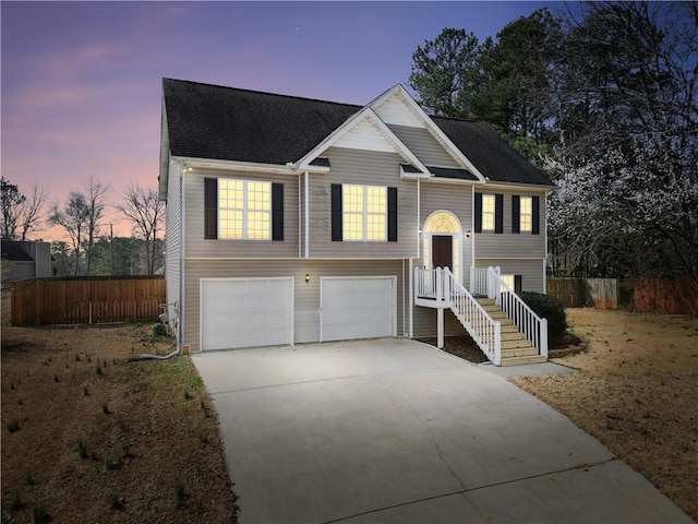 raised ranch featuring a shingled roof, driveway, an attached garage, and fence