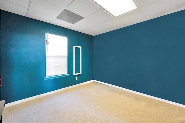 empty room with carpet flooring, a paneled ceiling, and baseboards