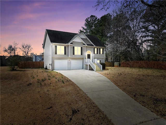 raised ranch featuring concrete driveway, an attached garage, and fence