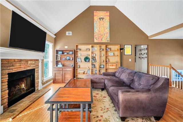 living room featuring visible vents, high vaulted ceiling, a warm lit fireplace, and wood finished floors