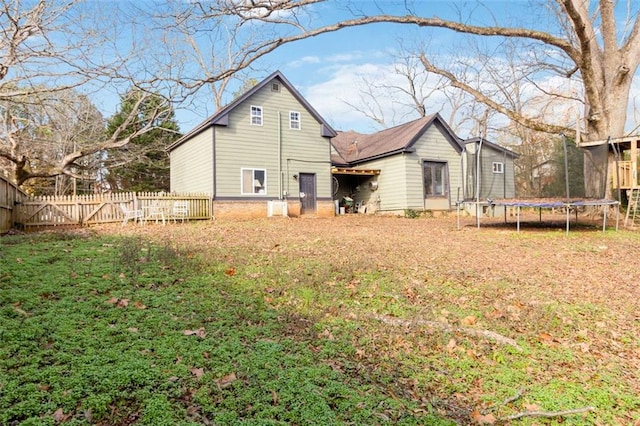 back of property featuring a trampoline and a lawn