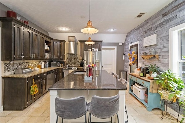 kitchen with pendant lighting, wall chimney range hood, sink, dark brown cabinets, and stainless steel appliances