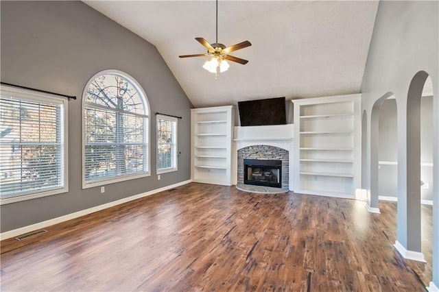 unfurnished living room featuring ceiling fan, a stone fireplace, dark wood-type flooring, and built in shelves