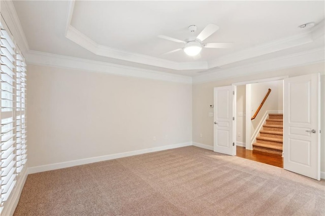 unfurnished room with a tray ceiling, crown molding, baseboards, and light carpet