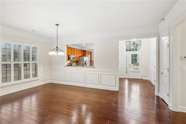 unfurnished living room with dark wood-type flooring, a decorative wall, crown molding, and a chandelier