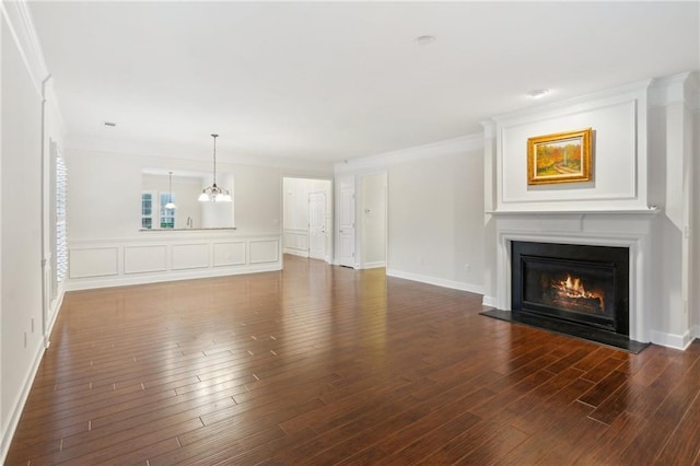 unfurnished living room with wood finished floors, a warm lit fireplace, ornamental molding, a decorative wall, and a notable chandelier