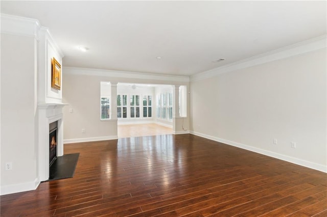 unfurnished living room with baseboards, ornate columns, a fireplace with flush hearth, hardwood / wood-style flooring, and crown molding