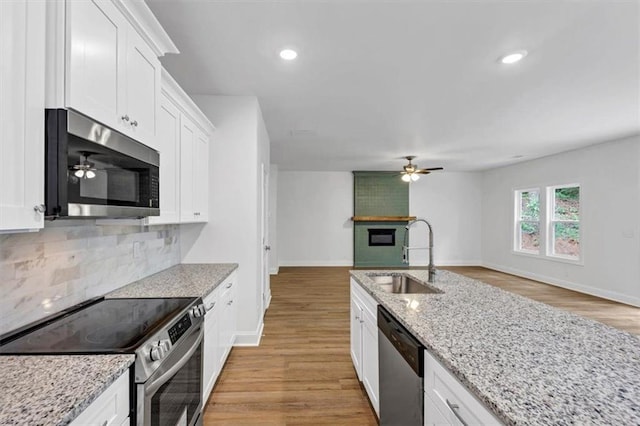 kitchen with a ceiling fan, a sink, light wood finished floors, backsplash, and stainless steel appliances