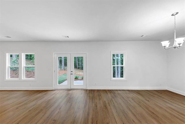unfurnished living room with baseboards, visible vents, wood finished floors, and a chandelier