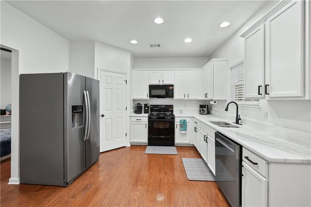 kitchen featuring black appliances, a sink, white cabinets, light wood finished floors, and light stone countertops