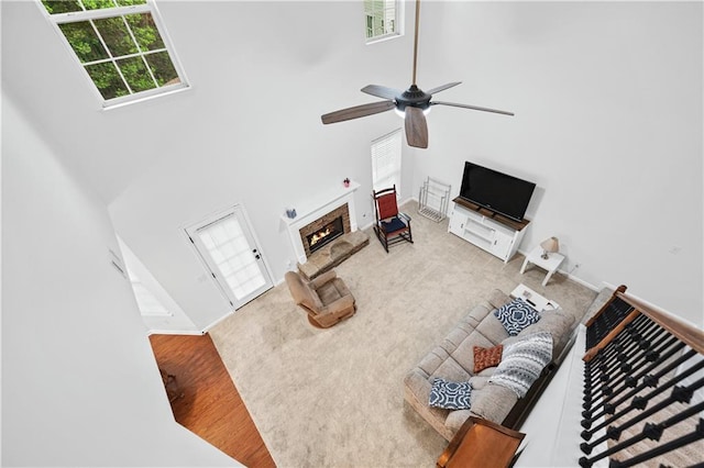 carpeted living room featuring a high ceiling, a ceiling fan, and a warm lit fireplace