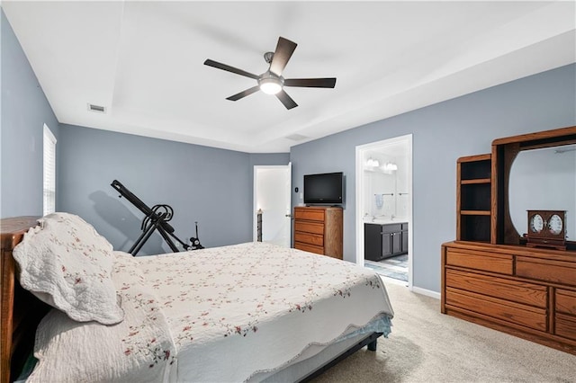 bedroom with a tray ceiling, light carpet, baseboards, ensuite bathroom, and ceiling fan