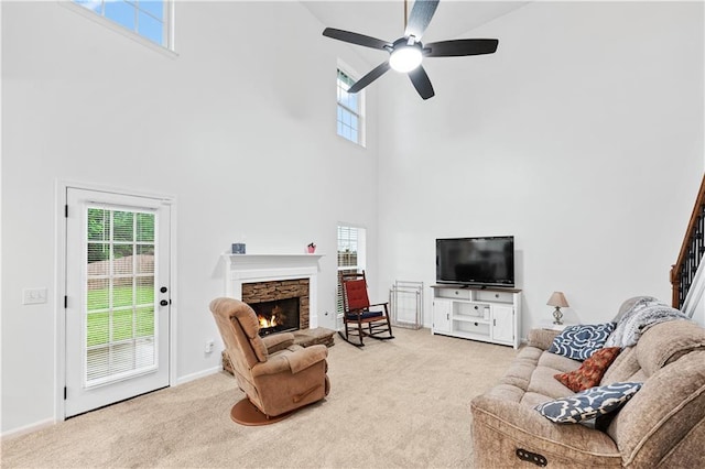 living area featuring a towering ceiling, carpet, healthy amount of natural light, a stone fireplace, and ceiling fan