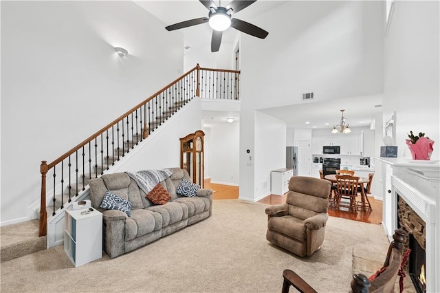 living area with stairway, high vaulted ceiling, a lit fireplace, ceiling fan, and baseboards