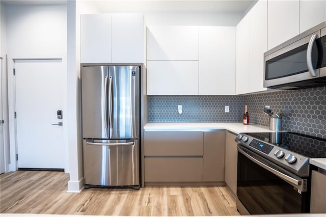 kitchen featuring appliances with stainless steel finishes, light hardwood / wood-style flooring, white cabinetry, and tasteful backsplash