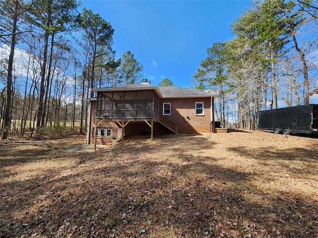 back of house with stairway, a sunroom, brick siding, and a chimney