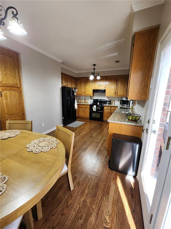 kitchen featuring a sink, dark wood-style floors, black appliances, brown cabinetry, and crown molding