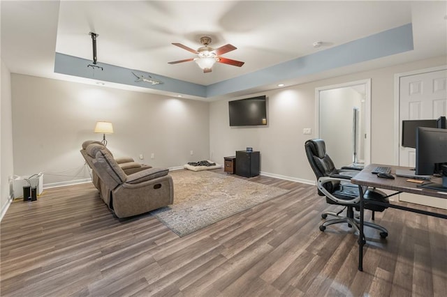 home office with ceiling fan, a raised ceiling, and wood-type flooring