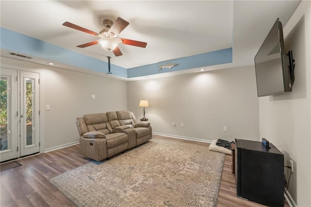 living room with wood-type flooring, a tray ceiling, and ceiling fan