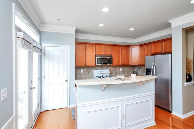 kitchen with stainless steel appliances, light countertops, brown cabinetry, light wood-style floors, and ornamental molding