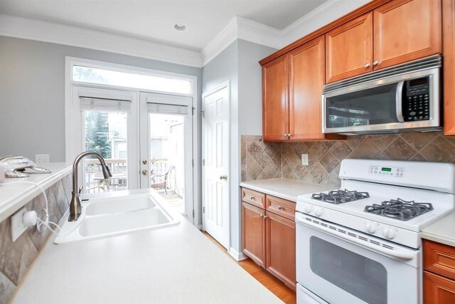 kitchen featuring white gas range oven, ornamental molding, backsplash, wood-type flooring, and sink