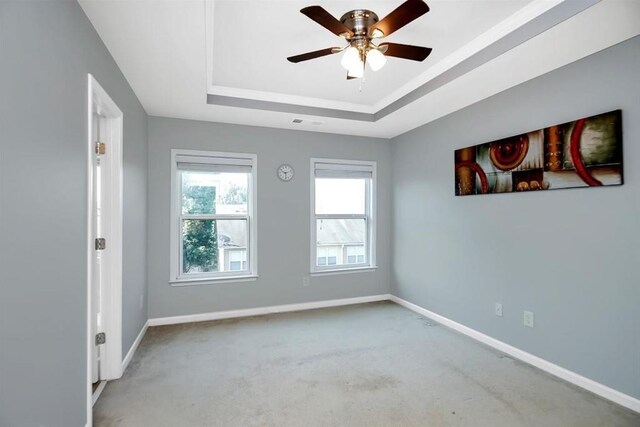 empty room featuring a raised ceiling, ceiling fan, and carpet flooring