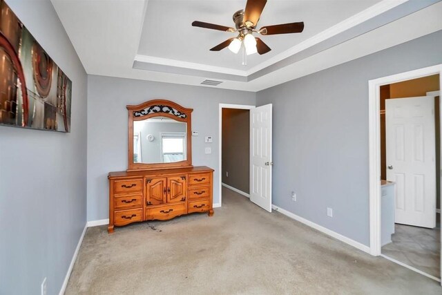 unfurnished bedroom featuring a raised ceiling, ceiling fan, ensuite bathroom, and light colored carpet