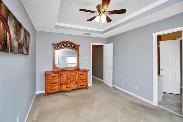 unfurnished bedroom with a tray ceiling, light colored carpet, visible vents, and baseboards