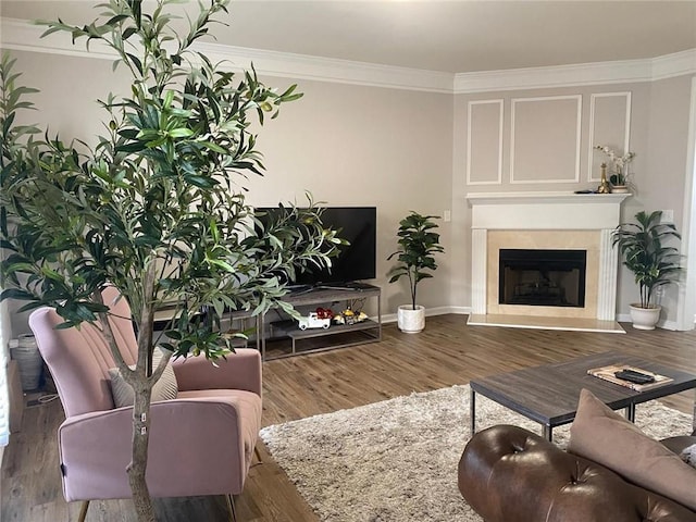 living area featuring baseboards, a fireplace with raised hearth, crown molding, and wood finished floors