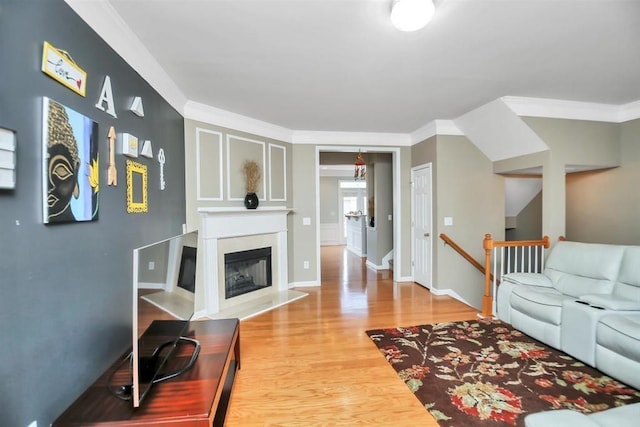 living area featuring baseboards, ornamental molding, a fireplace with raised hearth, and wood finished floors