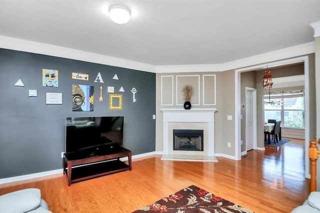 living area featuring a fireplace with raised hearth, crown molding, wood finished floors, and baseboards